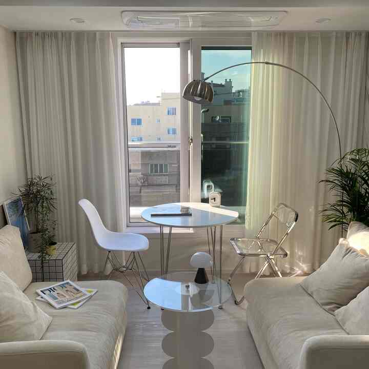 明るいホワイトトーンのリビング、2つのソファと透明な椅子、フロアランプが配置されたシンプルでモダンな空間