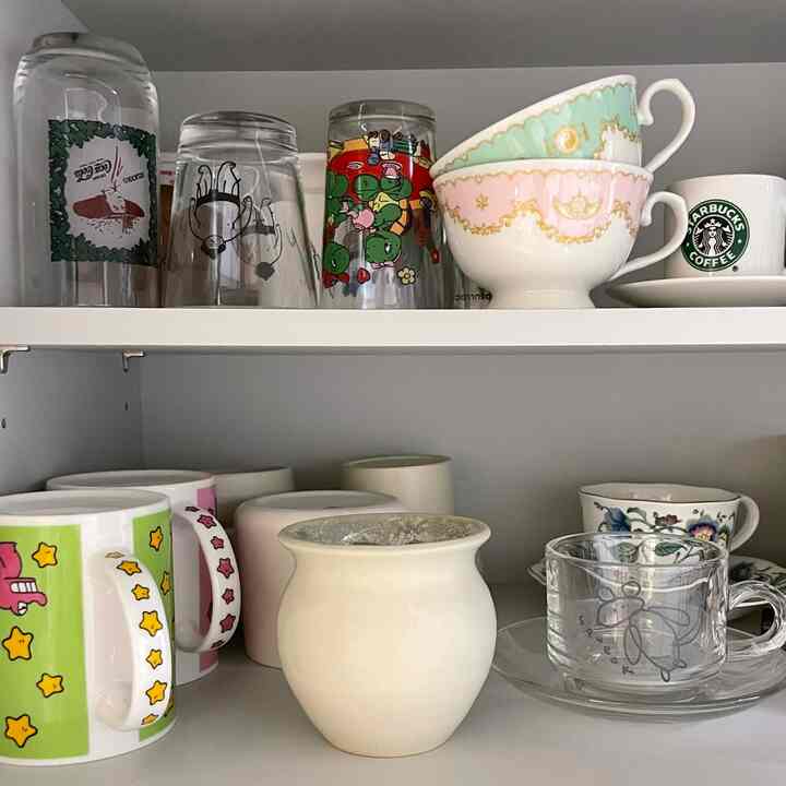 白を基調としたキッチン収納棚に、様々なパステルのボウルとマグカップが整然と並んだシンプルな雰囲気のインテリア