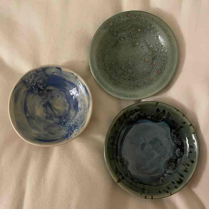 白い背景の上にさまざまな緑と青の色調の陶器の器が3つ並べられた、落ち着いた雰囲気の写真