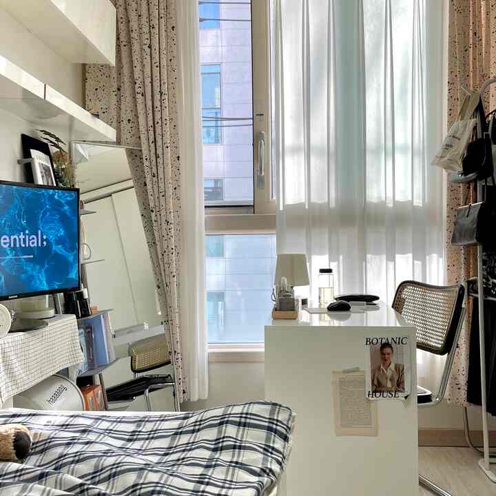 白とナチュラルカラーの寝室、デスクとラタンチェアが配置された落ち着いたワンルームインテリア