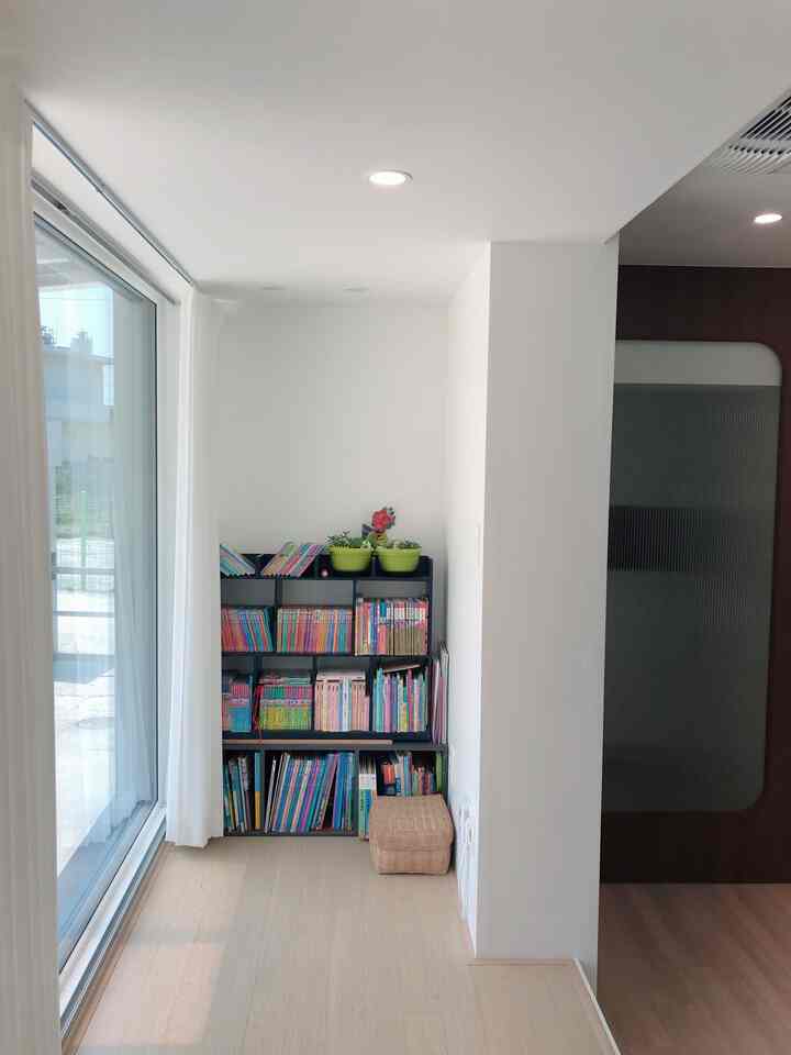 白い壁とベージュの木目調床が調和する子供部屋の一角、絵本棚とカーテンが自然な雰囲気を演出する空間