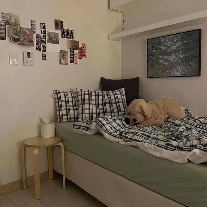 白い壁とナチュラルカラーの家具が配置された寝室、チェック柄の寝具と犬のぬいぐるみが置かれた印象的な空間