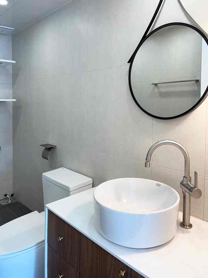 グレーのタイル壁と丸い洗面台、黒の丸鏡が配置されたモダンな白いバスルーム