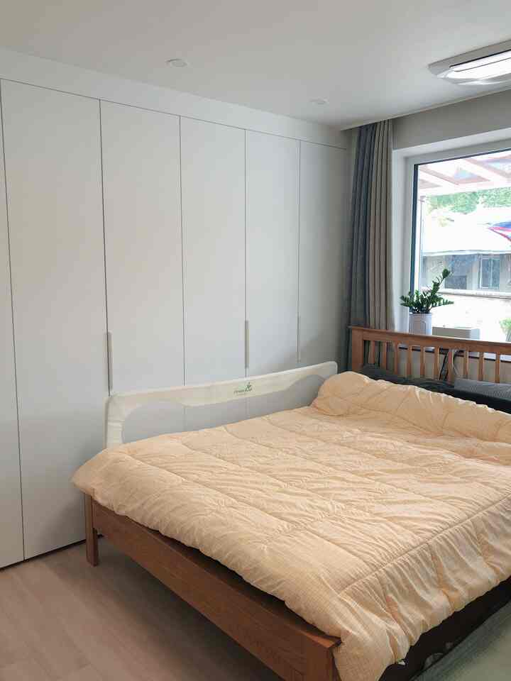 ナチュラルカラーの寝室、大きな木製ベッドとビルトインクローゼット、グレーのカーテンが配置された落ち着いた空間