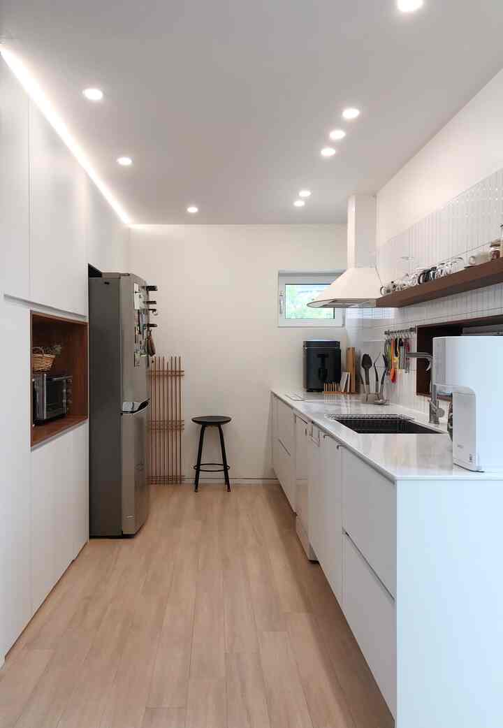 白を基調とした木目調の縦長キッチン、モダンで整ったレイアウトと収納アイデアが印象的な空間
