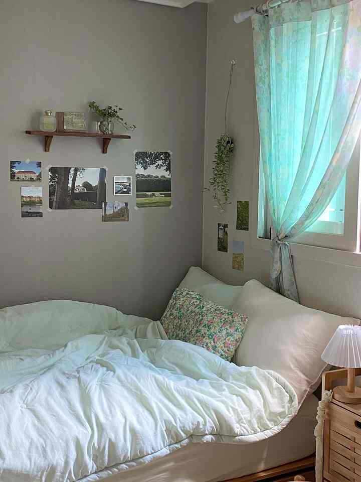 ナチュラルな色調の寝室、白いベッドと花柄の枕、木製の棚と小さなカーテンが配置された雰囲気のある空間