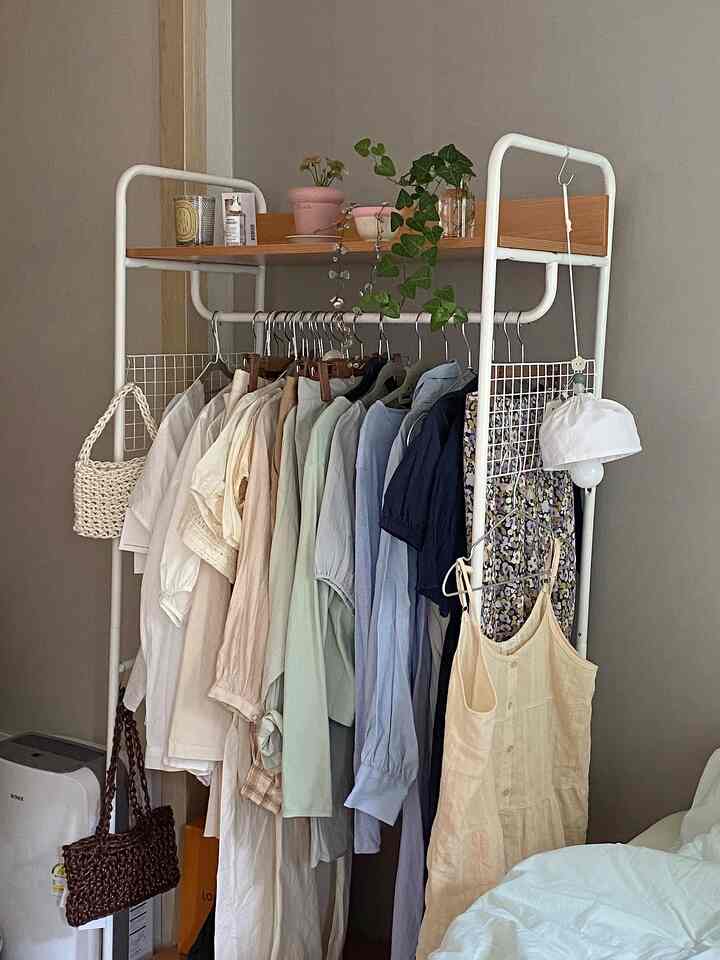 ナチュラルトーンの寝室空間、ホワイトスチールフレームと木製棚が調和したクローゼットと植物が配置された雰囲気のあるインテリア