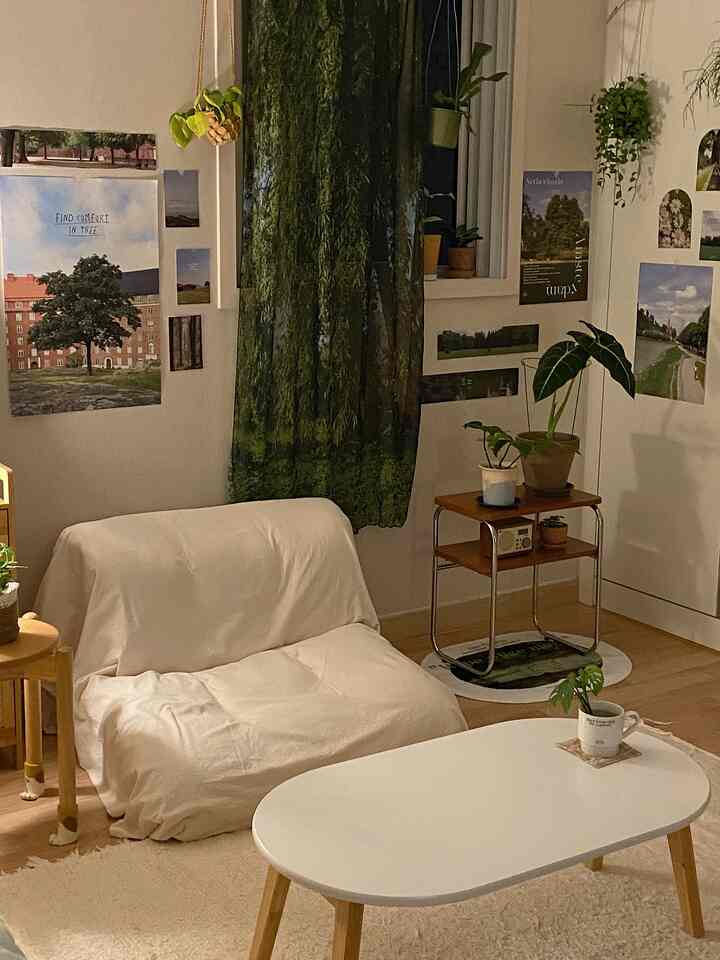 ナチュラルトーンの寝室、白いソファベッドと緑のファブリックカーテン、小さな鉄製ナイトテーブルと植物が配置された居心地の良い空間