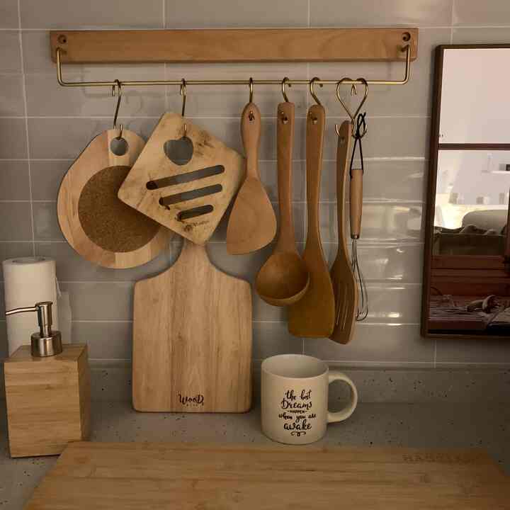 温かみのある木目調のキッチン、木製のまな板と調理器具が整然と掛けられ、マグカップとソープディスペンサーが配置された雰囲気のある空間