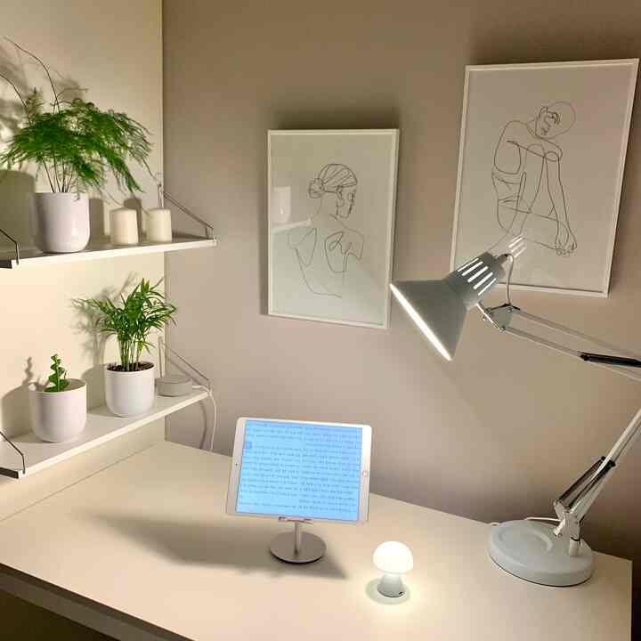 白とベージュのトーンが特徴のホームオフィス、机の上にタブレットと照明、壁の棚に植物が配置された印象的な作業空間