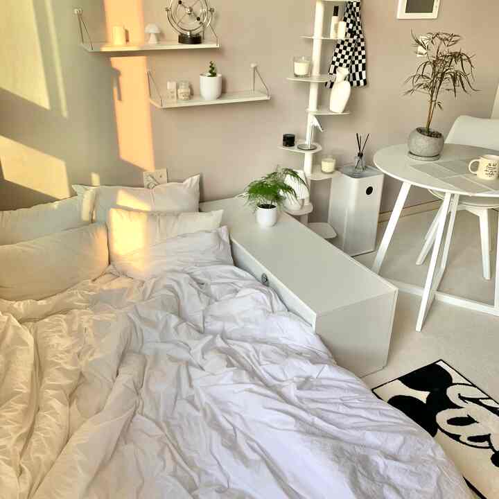 ホワイトとナチュラルな色調の寝室、白い寝具と円形テーブル、植物が配置された雰囲気のあるインテリア