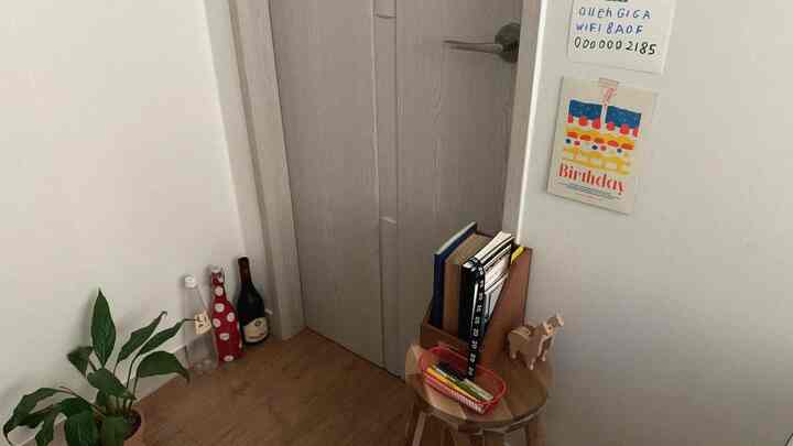 ナチュラルカラーの寝室のコーナー、小さなスツールの上に本棚と植物が配置された雰囲気のある空間