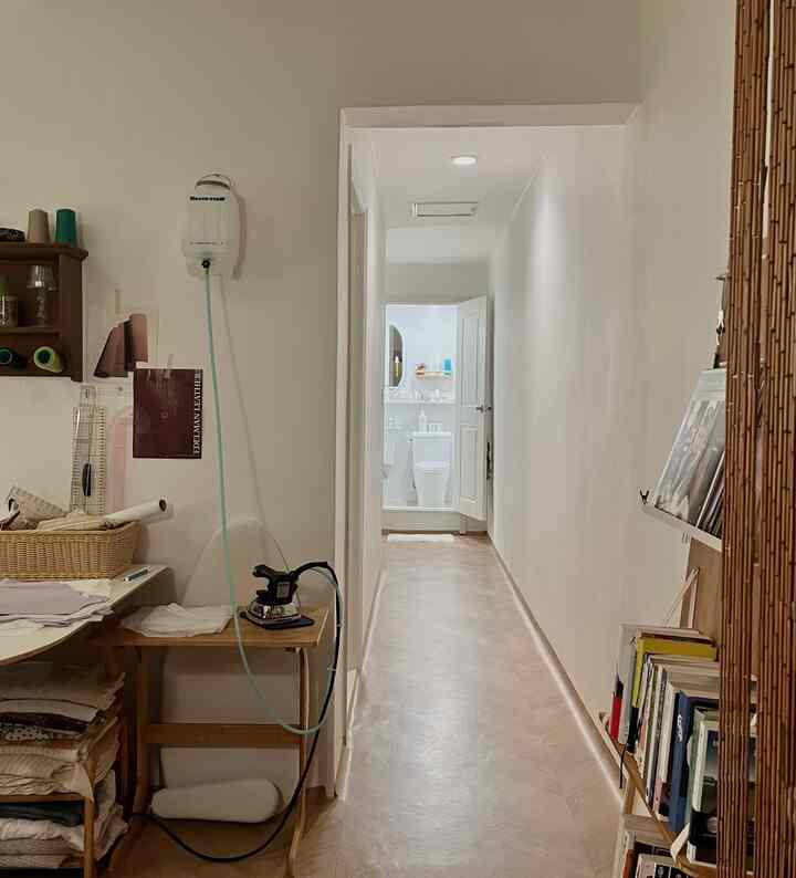 ナチュラルな木目調とホワイトの色調の細長い廊下、左側に木製デスクと収納、右側に本棚と竹製ラックが配された整った空間