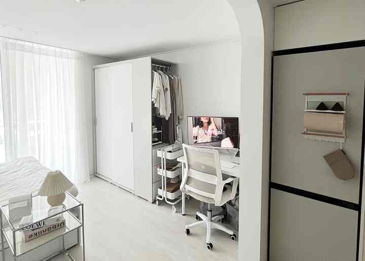 白を基調としたワンルームの寝室とコンパクトなワークスペースが配置された清潔感あるインテリア空間