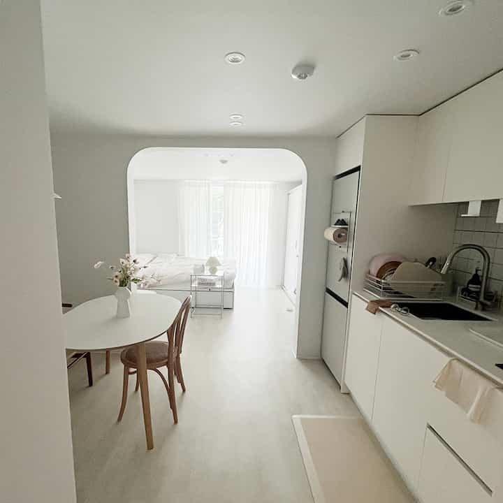 明るいホワイトトーンのキッチンとアーチ型の開口部から見える寝室があるスタジオタイプのインテリア