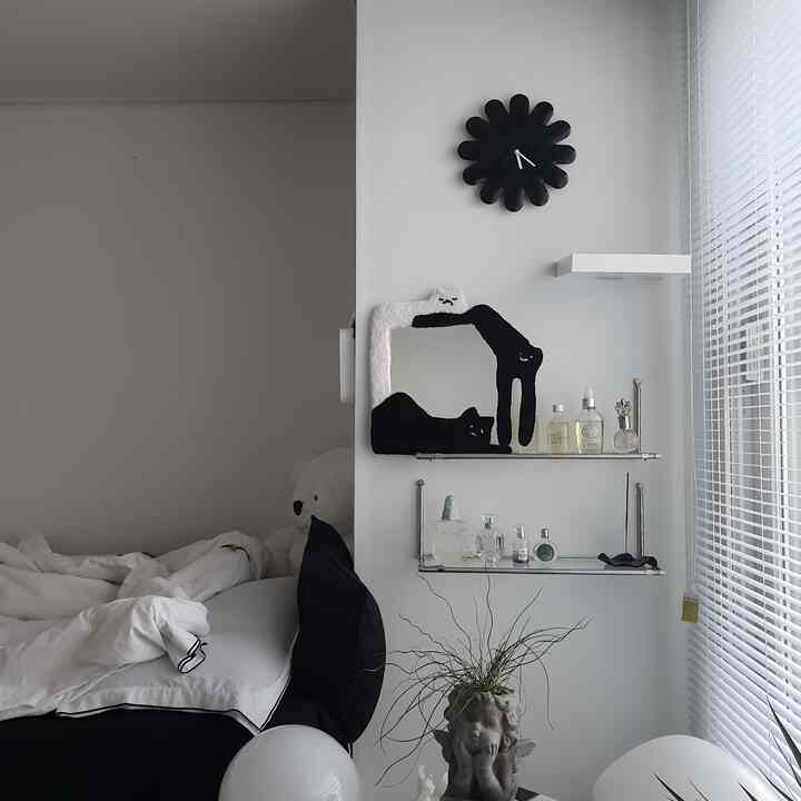 白と黒のトーンの寝室、壁時計とタフティングミラー、棚が整然と配置されたモダンな雰囲気のインテリア