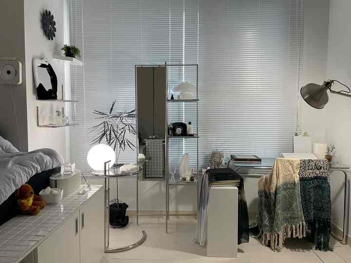 白とシルバーのトーンでまとめられた小さなワンルームの寝室、モダンなデスクとクローム家具が配置された印象的な空間