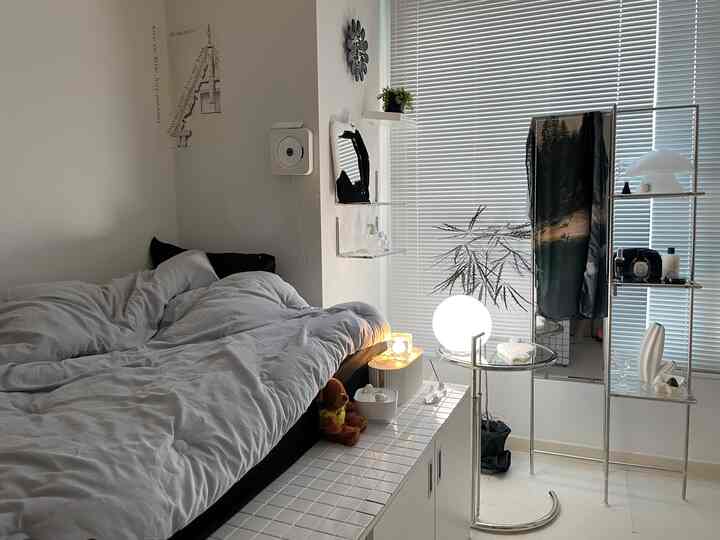 モノトーンとシルバーの色調を持つ寝室、白いブラインドと全身鏡、明るいムードライトが調和した清潔で現代的なインテリア