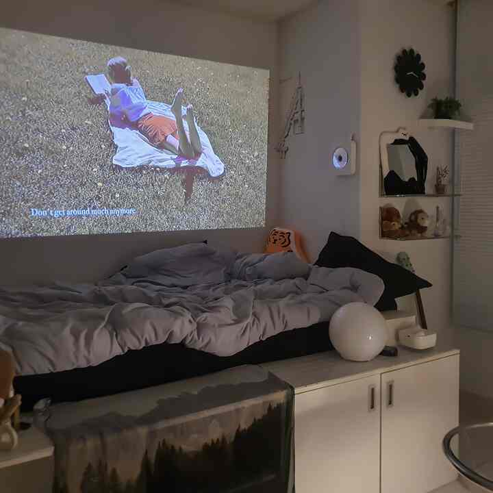 モノトーンの寝室にプロジェクタースクリーンと整ったベッド、収納キャビネットが配置されたシンプルな雰囲気のインテリア