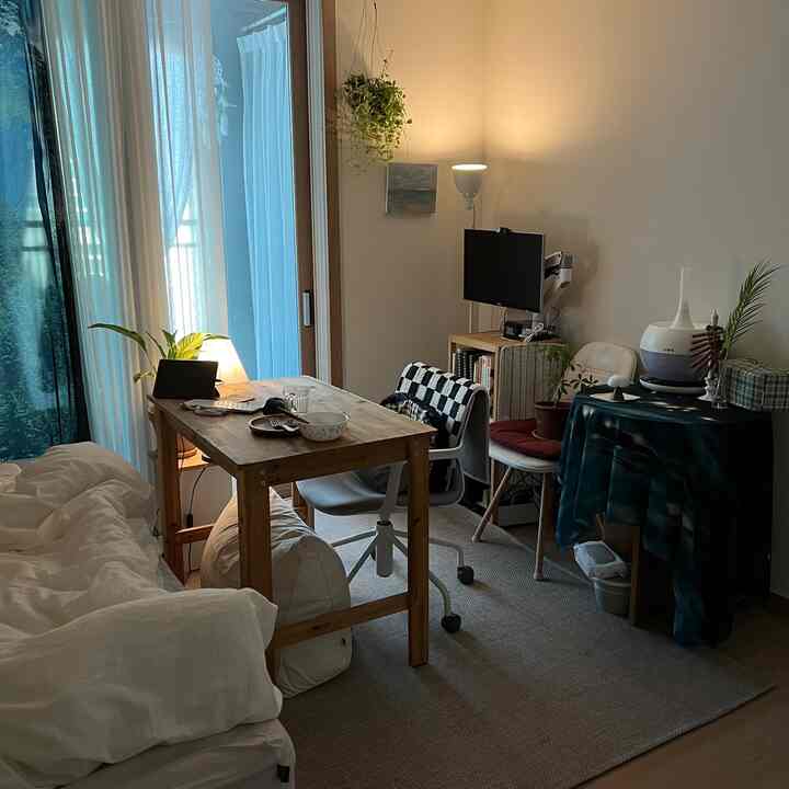 ベージュと木目調の狭い寝室兼ホームオフィス、木製デスクとオフィスチェア、ベッド、植物が配置された落ち着いた空間