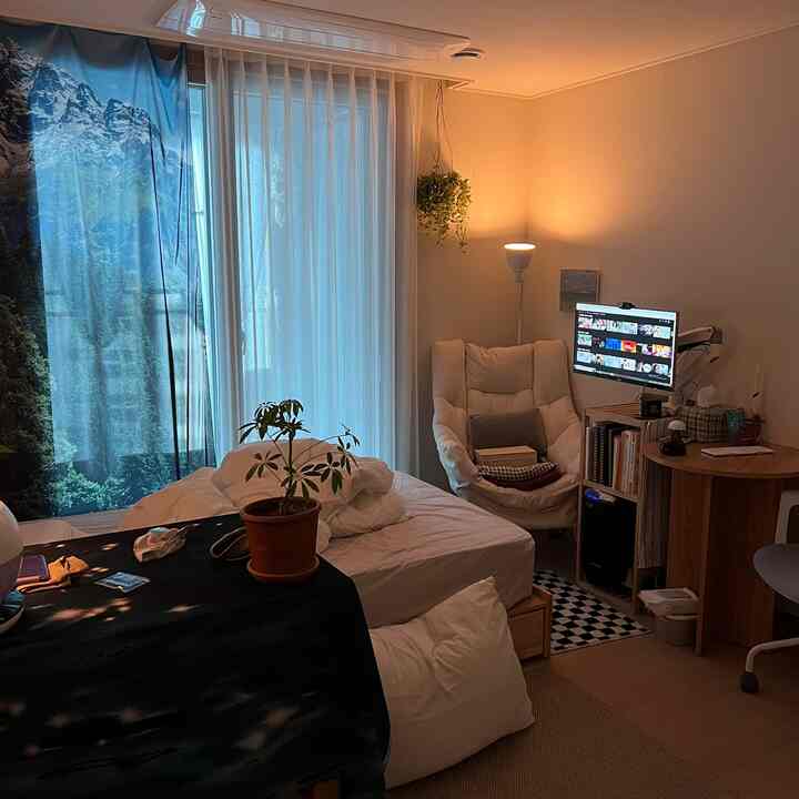 白とナチュラルカラーの寝室、コンピューターデスクとアームチェアが配置された落ち着いた一人暮らしの空間