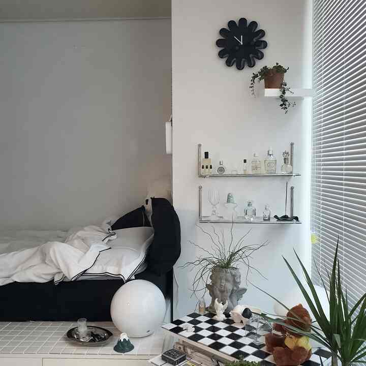 ホワイトとグレーのトーンの寝室、モノトーンの家具とブラインド、壁時計、植物が配置されたシンプルで雰囲気のあるインテリア