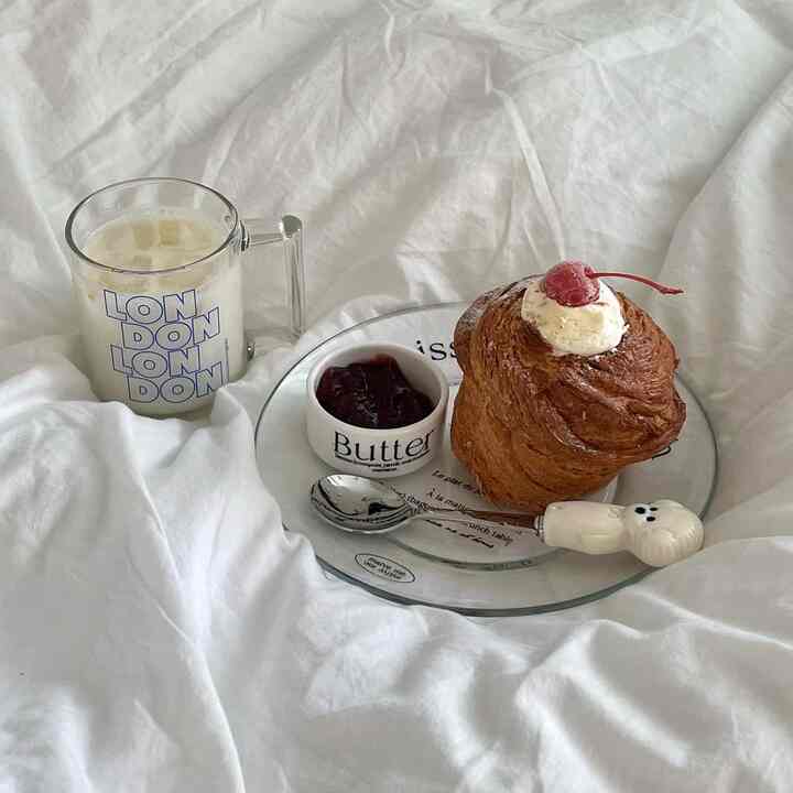 白い寝具の上にマグカップとサクサクのペストリー、ソースボウルが置かれた雰囲気のある寝室