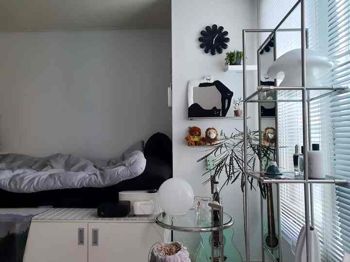 ホワイトとブラックのトーンでまとめられた狭い寝室、 高いベッドとメタルシェルフ、壁掛け時計がモダンな印象のインテリア