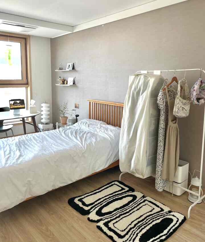 ナチュラルトーンのワンルーム寝室、木製ベッドと白い寝具、ハンガーラックが配置されたすっきりとした空間