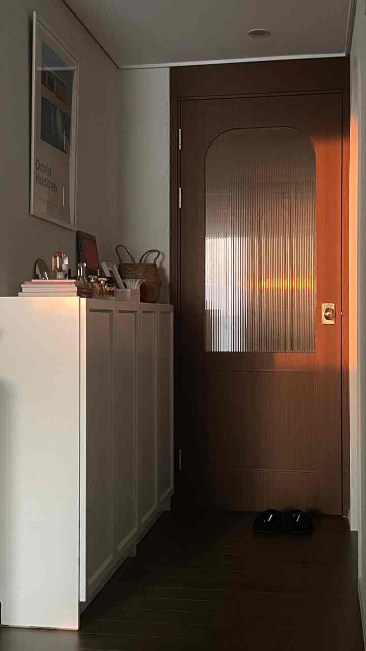 暖かい木目調の中扉と白い収納棚が配置されたアパートの玄関廊下、落ち着いた雰囲気のあるインテリア