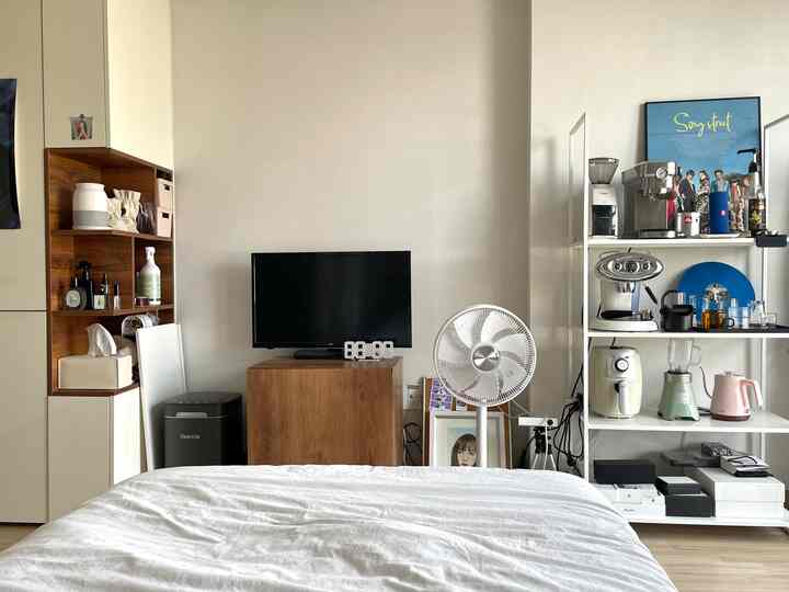 ホワイトと木目調が調和するワンルーム寝室、ベッド前にテレビ台とコーヒー家電が配置された雰囲気のあるインテリア