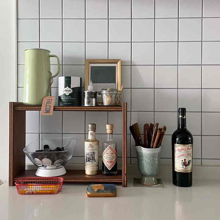 白いタイル壁と木製の棚が配置されたナチュラルなキッチン空間、調理器具とワインボトルが整然と並ぶ印象的なインテリア