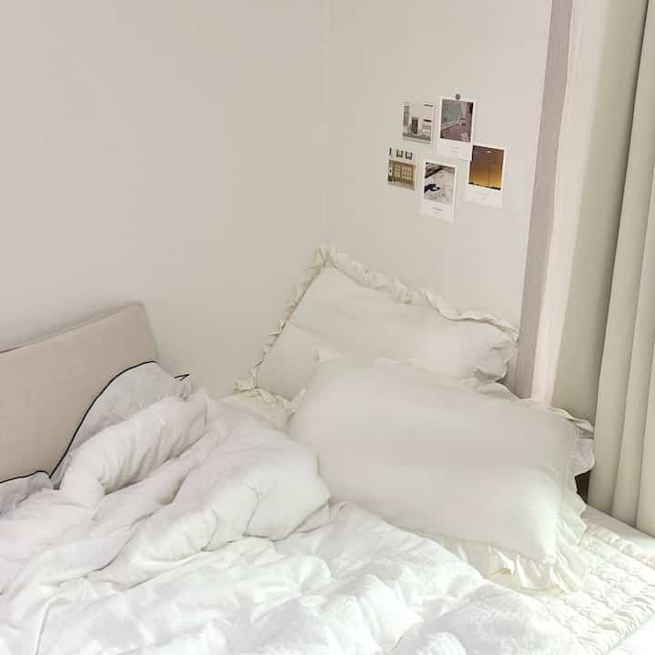 暖かいホワイトトーンの寝室、ふんわりとしたホワイトの寝具とフリル付き枕が配置された雰囲気のあるインテリア