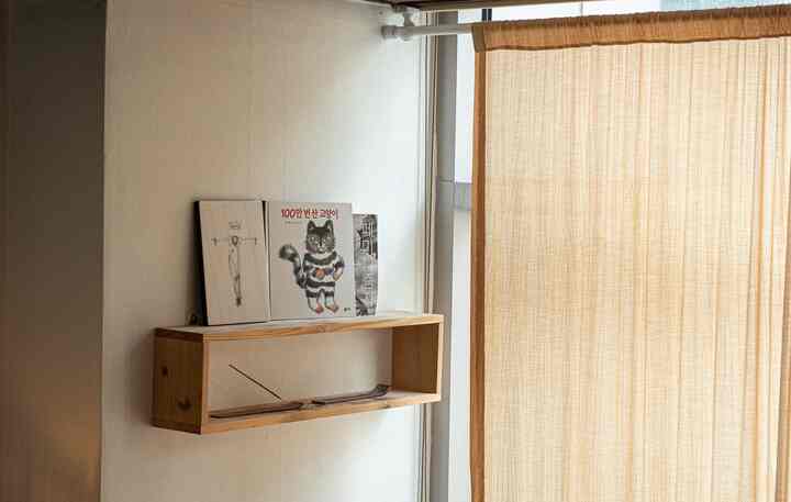 ホワイトの壁と木目調の木製棚、ベージュ色のブラインドが調和したナチュラルな読書空間のインテリア