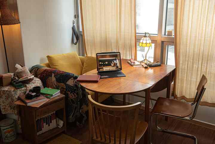 自然なベージュ色のカーテンがある小さな二人用ダイニング、木製のテーブルと椅子、黄色いクッションで暖かみのある雰囲気のインテリア