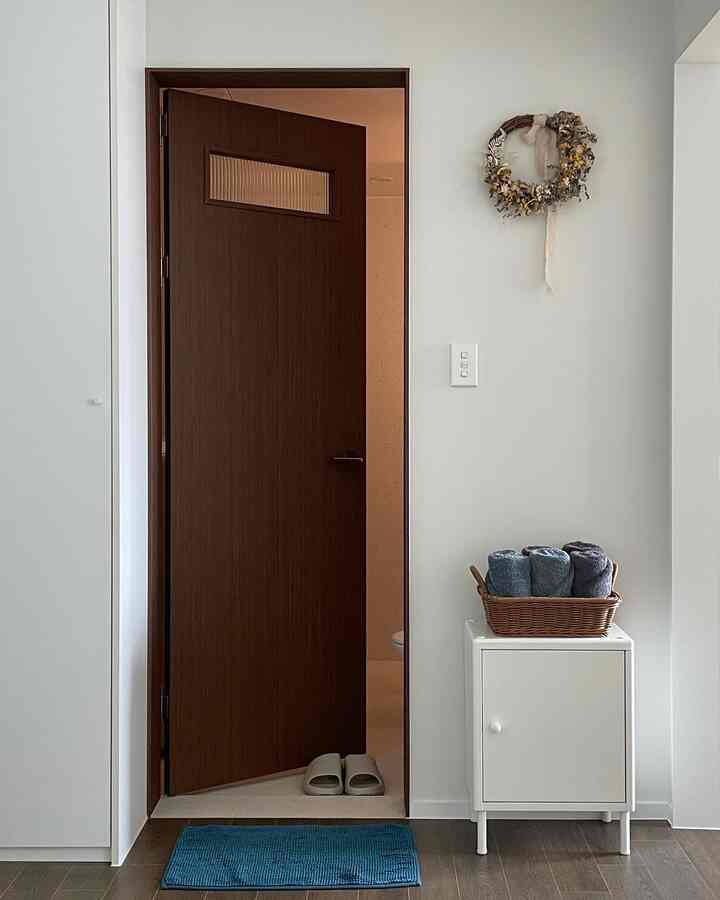 白と茶色のトーンが調和したバスルームの入り口、バスマットとタオルが置かれたシンプルで居心地の良い空間