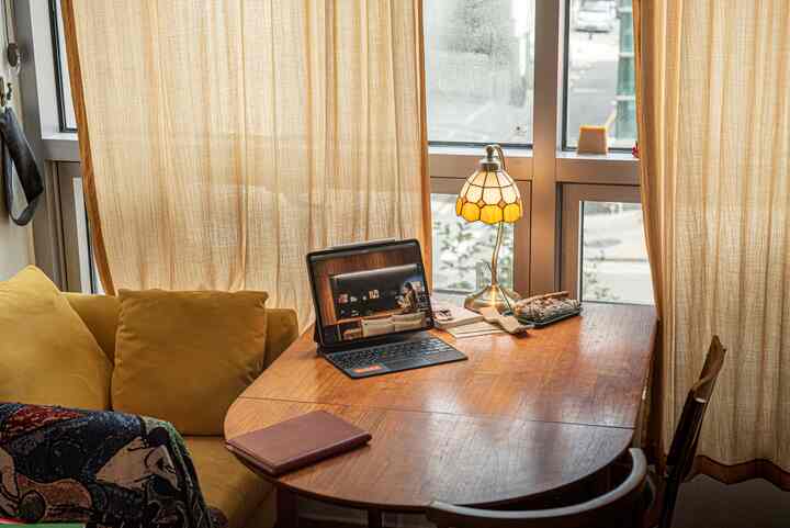 ベージュのカーテンと黄色いソファ、木製ダイニングテーブルのある居心地の良いホームオフィス兼読書スペース