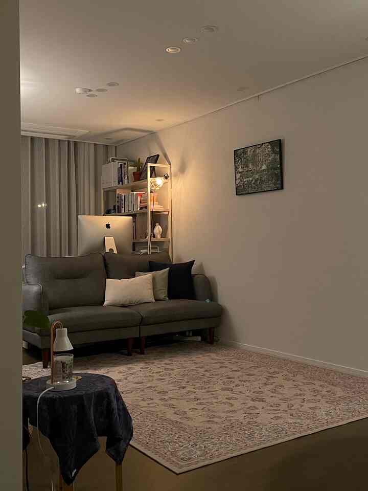 暖かい黄色の照明が灯るリビング、グレーのソファとペルシャ絨毯が配置された居心地の良い空間