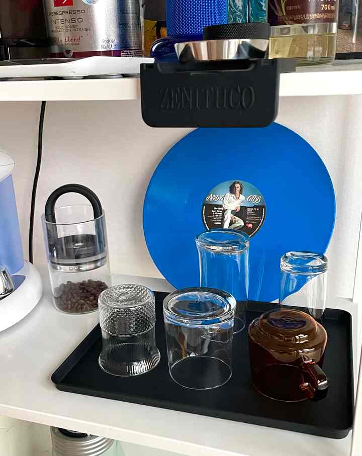 ホワイトとブラックのトーンのミニホームカフェ、黒いトレイの上にグラスやマグカップが置かれ、青いレコード盤が壁に飾られている印象的な空間