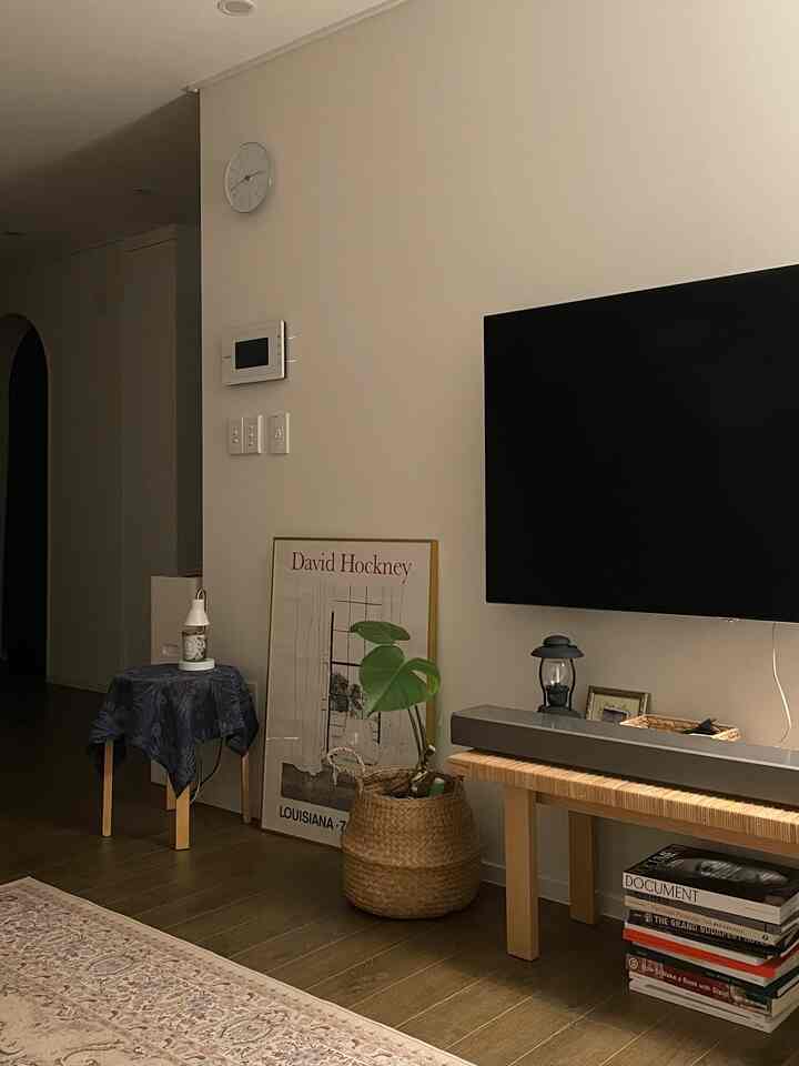 ナチュラルなトーンのリビング、ゴールドの額縁とラタンバスケットの植物が調和する落ち着いた空間