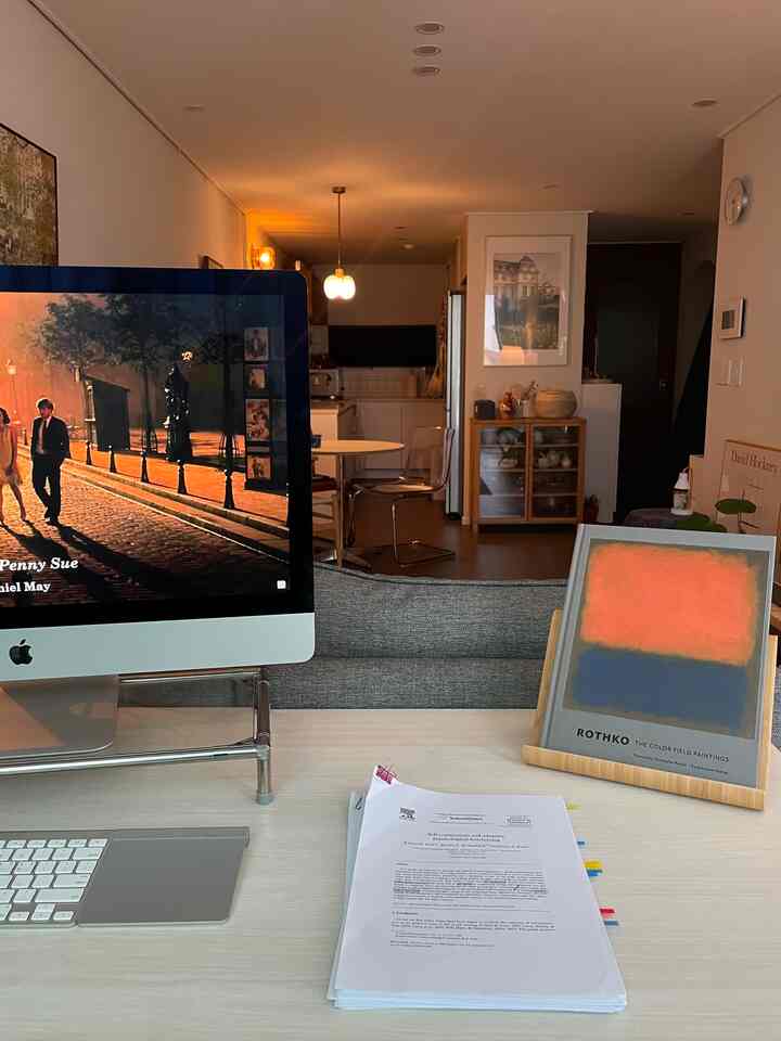明るい木目調の色合いが広がるリビングとキッチンが見えるホームオフィス空間、iMacと整理されたデスクが配置されている