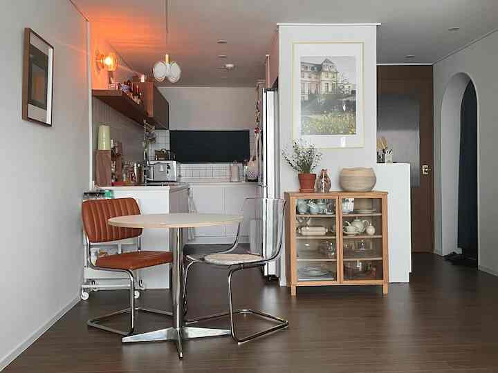 ホワイトの壁とブラウンの木製床が調和する、小さなキッチンと円形ダイニングテーブルを配したナチュラルモダンな空間