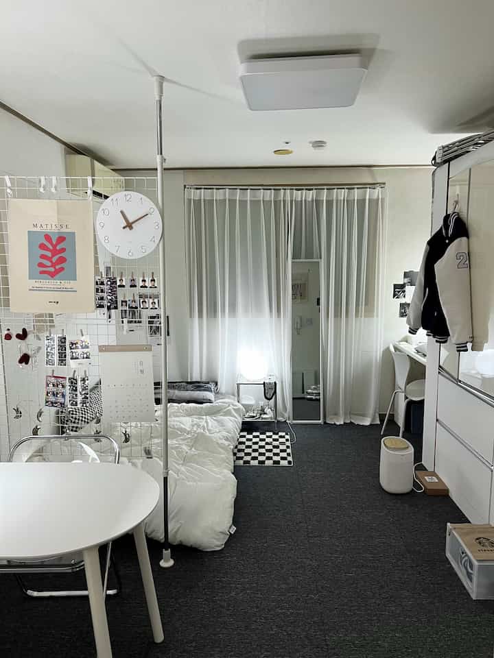 白とダークグレーのモノトーンの一人暮らし向け寝室とダイニングスペース、パーティションとカーペットが調和した雰囲気のある空間