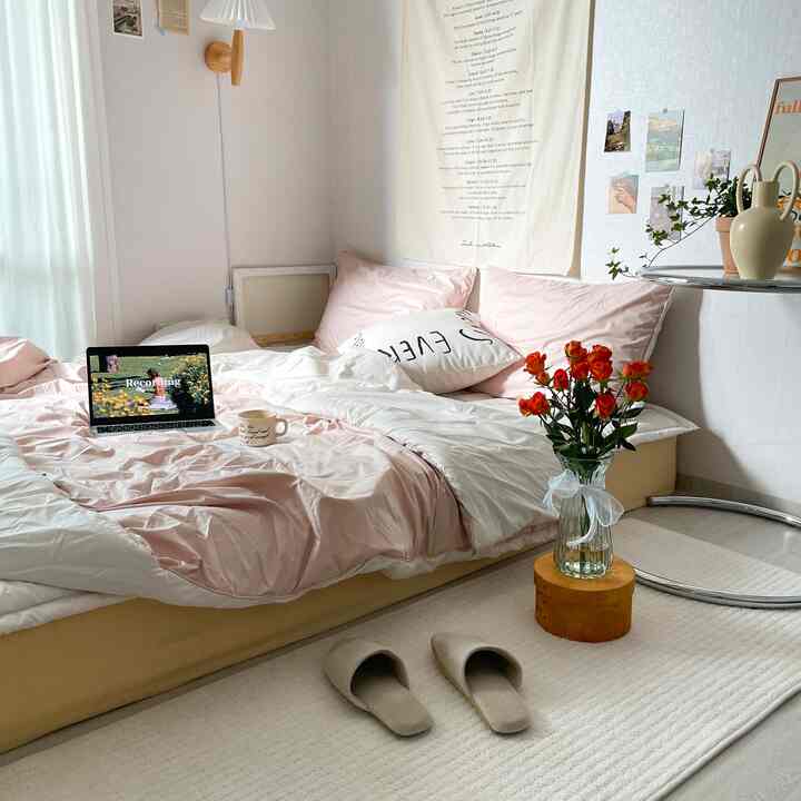 柔らかいピンクとベージュ調の寝室、心地よい寝具と小さな花瓶が配置された雰囲気のあるインテリア