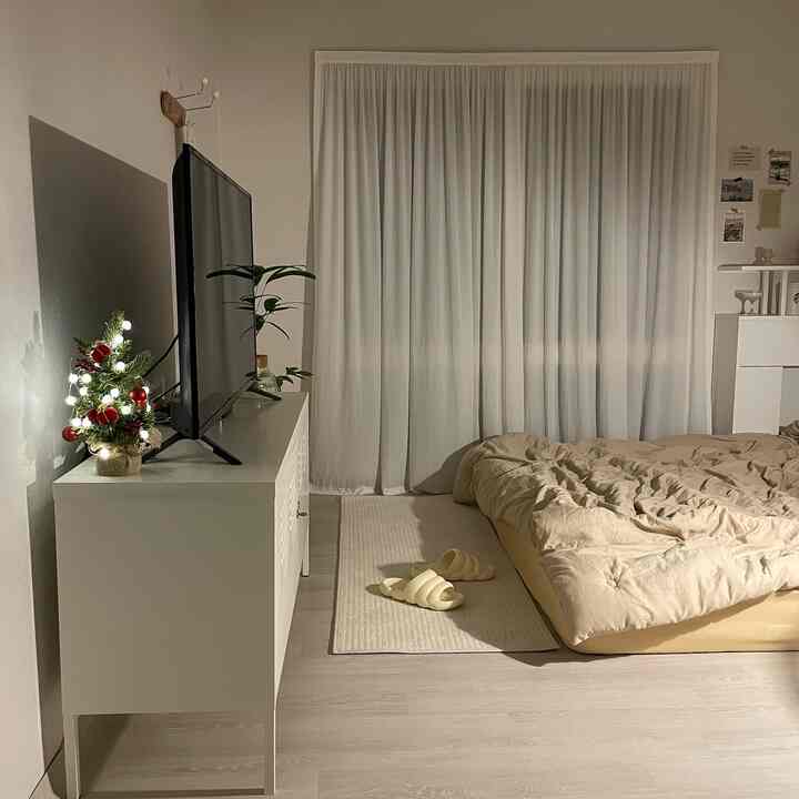 白とベージュの落ち着いた寝室、キャビネットの上にミニクリスマスツリーが灯り、くつろげる寝具とスリッパが配置された雰囲気のある空間