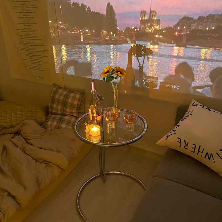 暖かいブラウンとホワイトの色調の寝室、丸いサイドテーブルにワイングラスとキャンドルが置かれ、壁に夕暮れの川の風景がプロジェクターで映し出された雰囲気のある空間