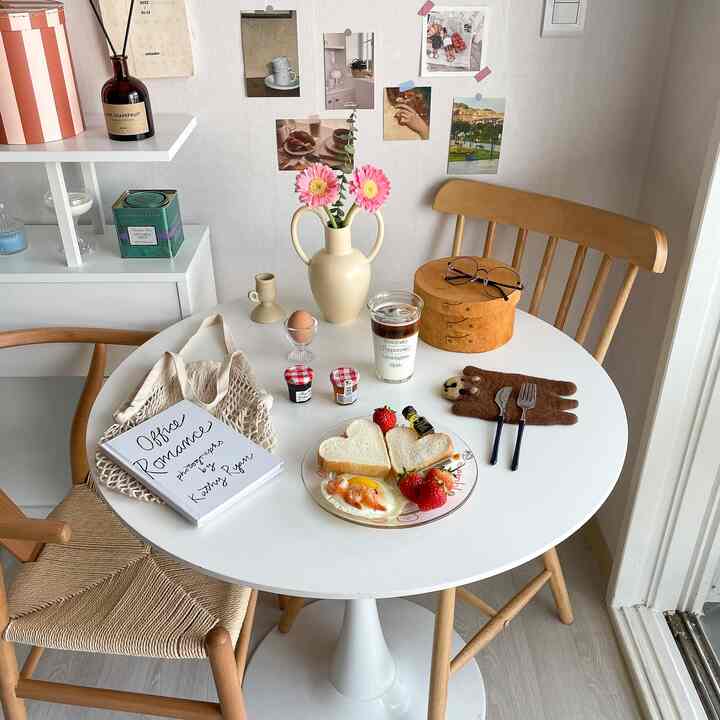 白と木目調の調和が取れたキッチン空間、円形ダイニングテーブルと自然な花飾りが印象的なホームカフェの雰囲気を演出している。