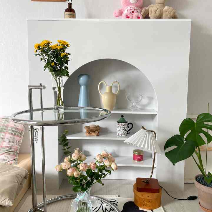 ホワイトとブラウンのトーンのリビング、アーチ型の暖炉コンソールと多彩なオブジェ、木製のフロアランプが調和した雰囲気のあるインテリア