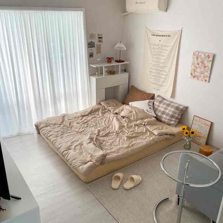 ベージュ調のナチュラルモダンな狭い寝室、低いベッドとラグ、白いカーテンが配置された落ち着いたシンプルな空間