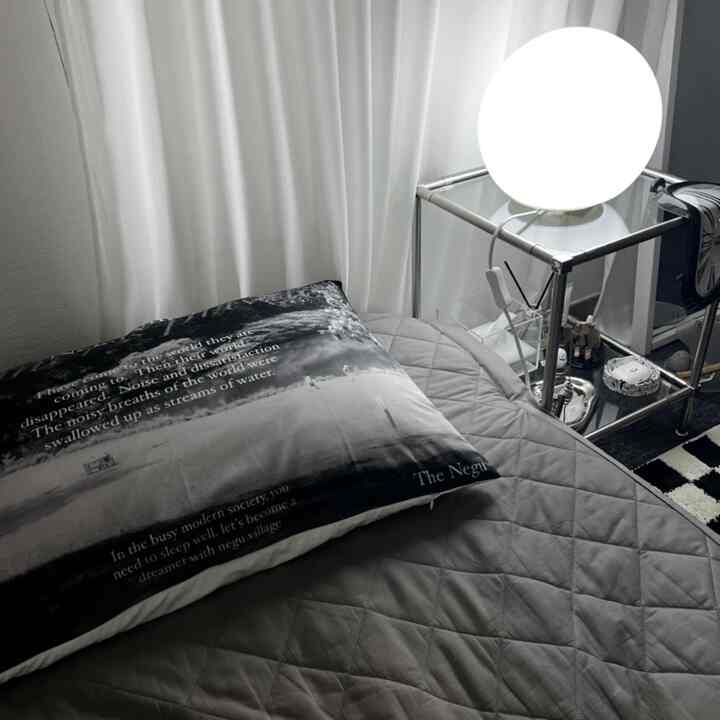 白黒のモノトーン寝室、文字入り枕とキルティングベッドカバー、透明なサイドテーブルと丸いフロアランプが配置された落ち着いた雰囲気のインテリア